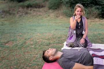 Woman with amulet doing hypnosis to calm lying man in nature