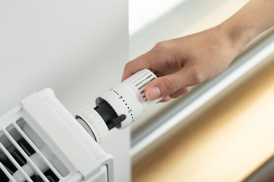 A woman adjusts the radiator thermostat to the economical mode of room heating