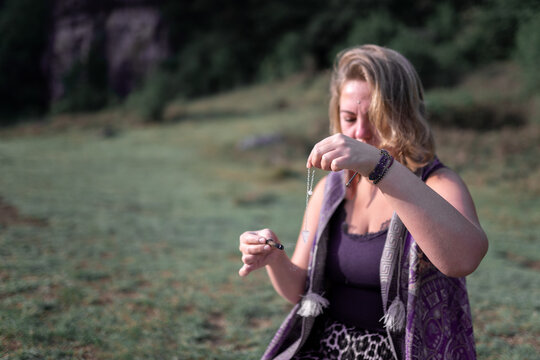 Calm woman with amulet necklace and burning stick sitting on meadow