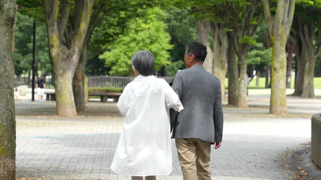 公園を歩くアジア人の高齢者夫婦の後ろ姿
