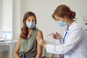 Female doctor or nurse in white coat giving arm injection to child. Happy teenage school girl in facemask getting flu, covid 19 or monkeypox vaccine during mass vaccination and immunization campaign