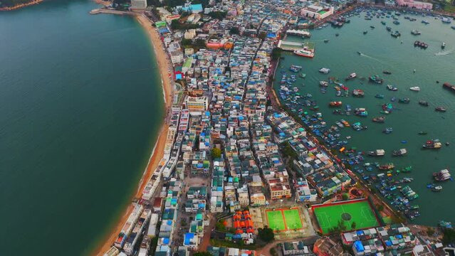 Drone shot traveling forward of a city built on an isthmus with an harbor and a popular beach during the day