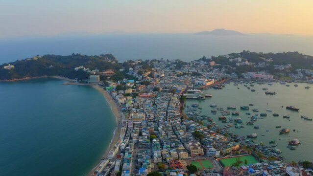 Drone shot traveling upward above a city built on an isthmus with an harbor and a popular beach during golden hour