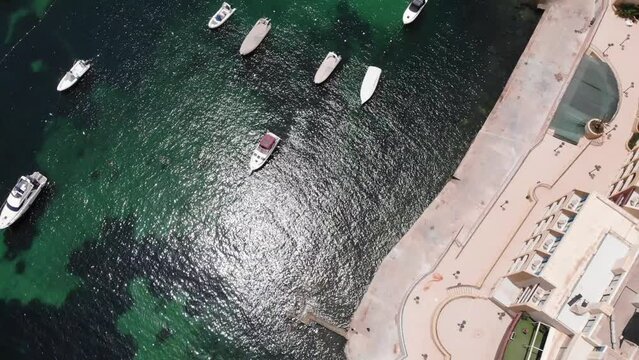 White small boats docked at Marina Hotel Corinthia Beach Resort in Saint George's Bay, St Julian's, Malta. Rising aerial drone view