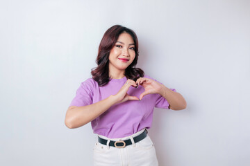 An attractive young Asian woman wearing a lilac purple t-shirt feels happy and a romantic shapes...