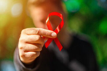 Young man with a red awareness ribbon for the fight against AIDS in his hand.Red ribbon on palms....