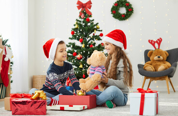 Fototapeta na wymiar Smiling children celebrate New Year at home unpack presents together in living room. Happy boy and girl kids have fun open gifts on Christmas morning, enjoy winter holidays festive atmosphere.