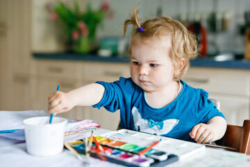 Cute happy little girl painting with water color on paper. Baby child learning different skills, creative leisure and activity for small children.