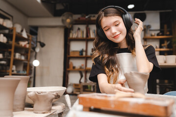 Beautiful young woman holding pottery instrument for scraping, smoothing, shaping and sculpting. Lady siting on bench with pottery wheel and making clay pot
