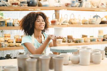 Creative afro American young woman artist molding clay on pottery wheel, Workshop in ceramic studio, clay making of a ceramic pot on the pottery wheel, hobby and leisure with pleasure concept