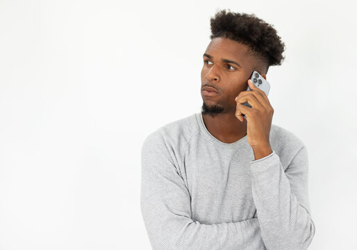 Portrait of confident African American man talking on smartphone. Young bearded man wearing white sweater using mobile phone and looking away. Mobile technology concept