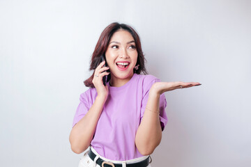 Smiling beautiful Asian woman pointing finger sideward to space while picking up phone call isolated white background