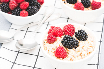 Healthy breakfast food - oatmeal porridge served with berries on white table background. Morning superfood porridge recipe