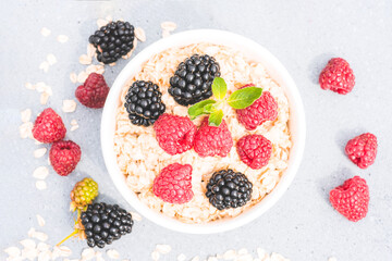 Top view on oatmeal porridge served with raspberries and blackberries on concrete table background. Morning superfood porridge recipe. Healthy breakfast