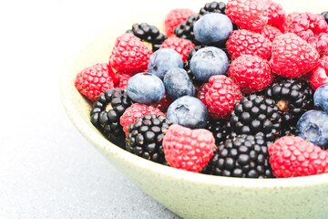 Bowl with freshly picked garden berries - raspberry, blackberry, blueberry. Healthy eating and dieting concept. Organic superfood snack. Summer berries background