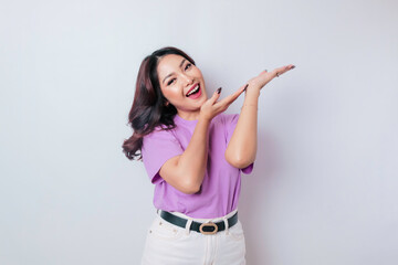 Obraz na płótnie Canvas Excited Asian woman wearing lilac purple t-shirt pointing at the copy space upside her, isolated by white background