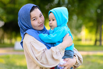 Cute young islamic kazakh woman hugging, playing with her little son, newborn boy. happy asian...