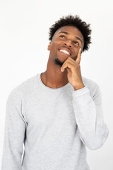 Fototapeta na wymiar Portrait of dreaming African American man wearing white sweater. Young bearded guy standing with hand on chin and thinking against white background. Dreaming and thinking concept