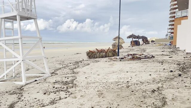 Aftermath of hurricane kay on a Mexican coastline with broken Palapas on the sand and a rescue tower