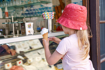 Cute little toddler girl choosing and buying ice cream in outdoor stand cafe. Happy preschool child...