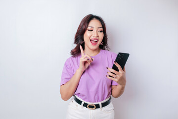 Naklejka premium A portrait of a happy Asian woman is smiling and holding her smartphone wearing a lilac purple t-shirt isolated by a white background