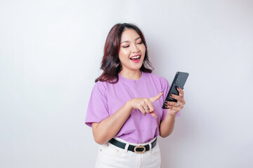 Fototapeta premium A portrait of a happy Asian woman is smiling and holding her smartphone wearing a lilac purple t-shirt isolated by a white background