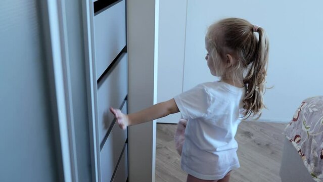 Cute little girl with blond hair cleans up the wardrobe