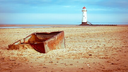 Old rusty piece of metal on an empty sandy beach with a lighthouse tower in the background