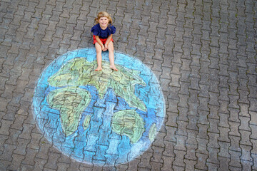 Little preschool girl with earth globe painting with colorful chalks on ground. Positive toddler...