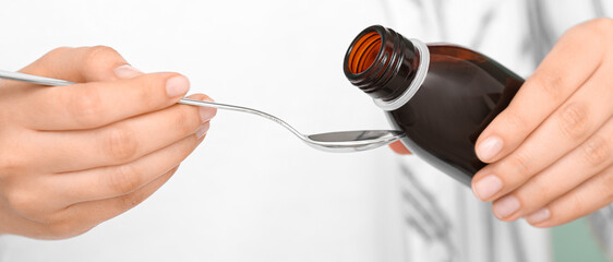 Woman pouring cough syrup from bottle into spoon, closeup