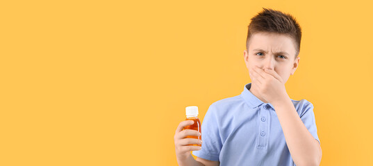 Ill little boy with cough syrup on yellow background with space for text