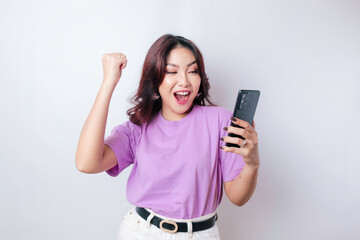 Fototapeta premium A young Asian woman with a happy successful expression wearing lilac purple shirt and holding smartphone isolated by white background