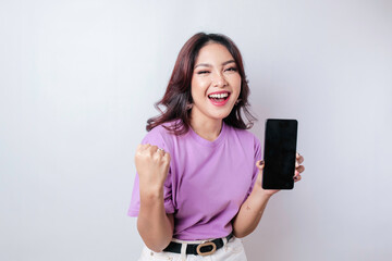 Naklejka premium A young Asian woman with a happy successful expression wearing lilac purple shirt and holding smartphone isolated by white background