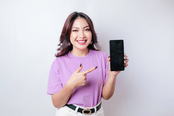 A portrait of a happy Asian woman is smiling and showing copy space on her smartphone wearing lilac purple shirt isolated by a white background