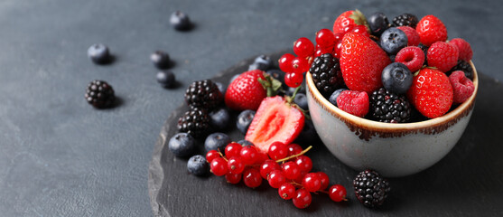 Bowl with different ripe berries on grey background