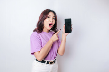 Surprised woman wearing a lilac purple shirt showing copy space on her smartphone, isolated by a white background