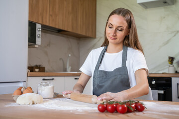 Woman in a grey chef's apron roll out the dough for preparing pancake. Woman rolls out dough. 
