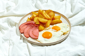 A fried egg with sausage and potatoes in a plate on a white sheet. English breakfast