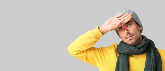Ill young man with clothespin on his nose against grey background with space for text