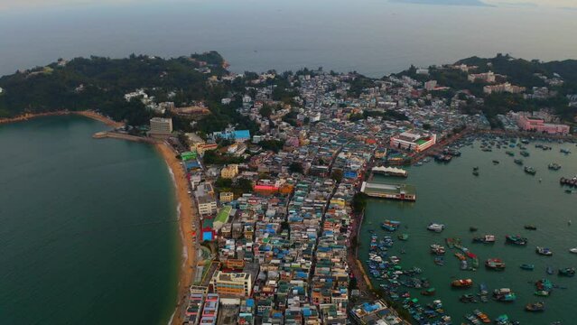 Drone shot traveling forward and panning down above a city built on an isthmus with an harbor and a popular beach during the day