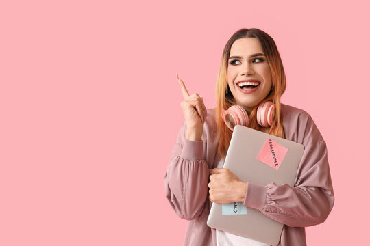 Transgender programmer with laptop pointing at something on pink background