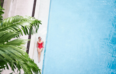 Enjoying suntan. Vacation concept. Top view of slim young woman in red swimsuit in the tropical swimming pool.