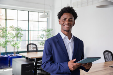 African-American office worker holding tablet, looking at camera. Medium shot of handsome young...
