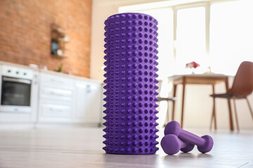 Naklejka premium Foam roller with dumbbells on floor in kitchen