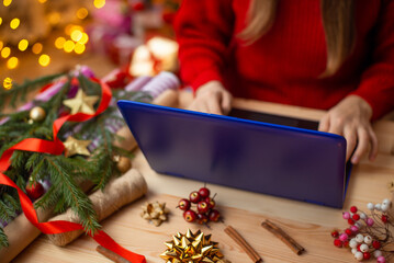 Close-up view of a girl working on modern laptop, preparing presents for friends. Christmas celebration, enjoying winter holidays time