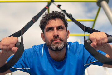 Caucasian man during workout with suspension TRX on the street. Fitness straps