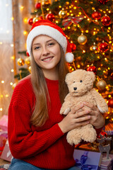 Young girl holding teddy bear near decorated Christmas tree. Christmas celebration at home, festive decorations around
