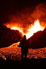 Vertical shot of a silhouette of a person watching lava flowing from a volcano at night in Iceland © Tomáš Malík/Wirestock Creators