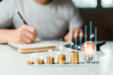 Man using calculator to calculate and taking notes and Stacking coins, light bulb on table. Saving money,accounting, investment, budgeting, and financial planning concept.