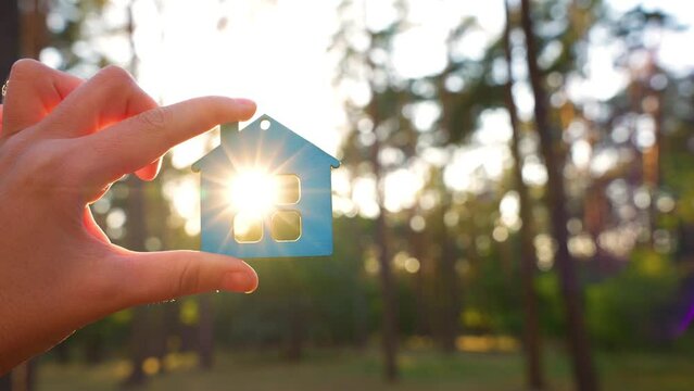 Flat house model in hand outdoors at sunrise